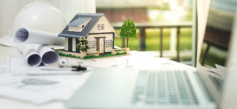 House model on blueprints next to a hard hat and a laptop