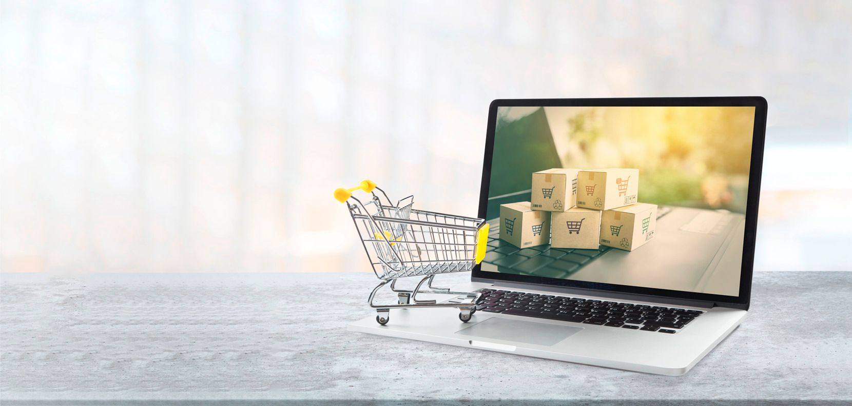 Miniature shopping cart next to a laptop showing shipping boxes